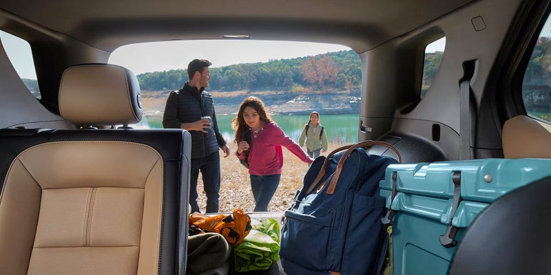 interior of the 2024 chevy equinox back seat and hatchback trunk open with father and daughters getting their gear and a lake in the background