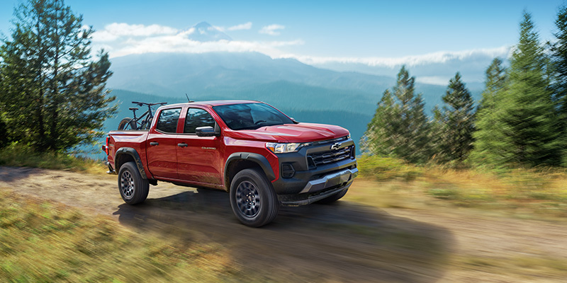 Red Chevrolet Colorado driving on a mountain dirt road with a bicycle in the bed.