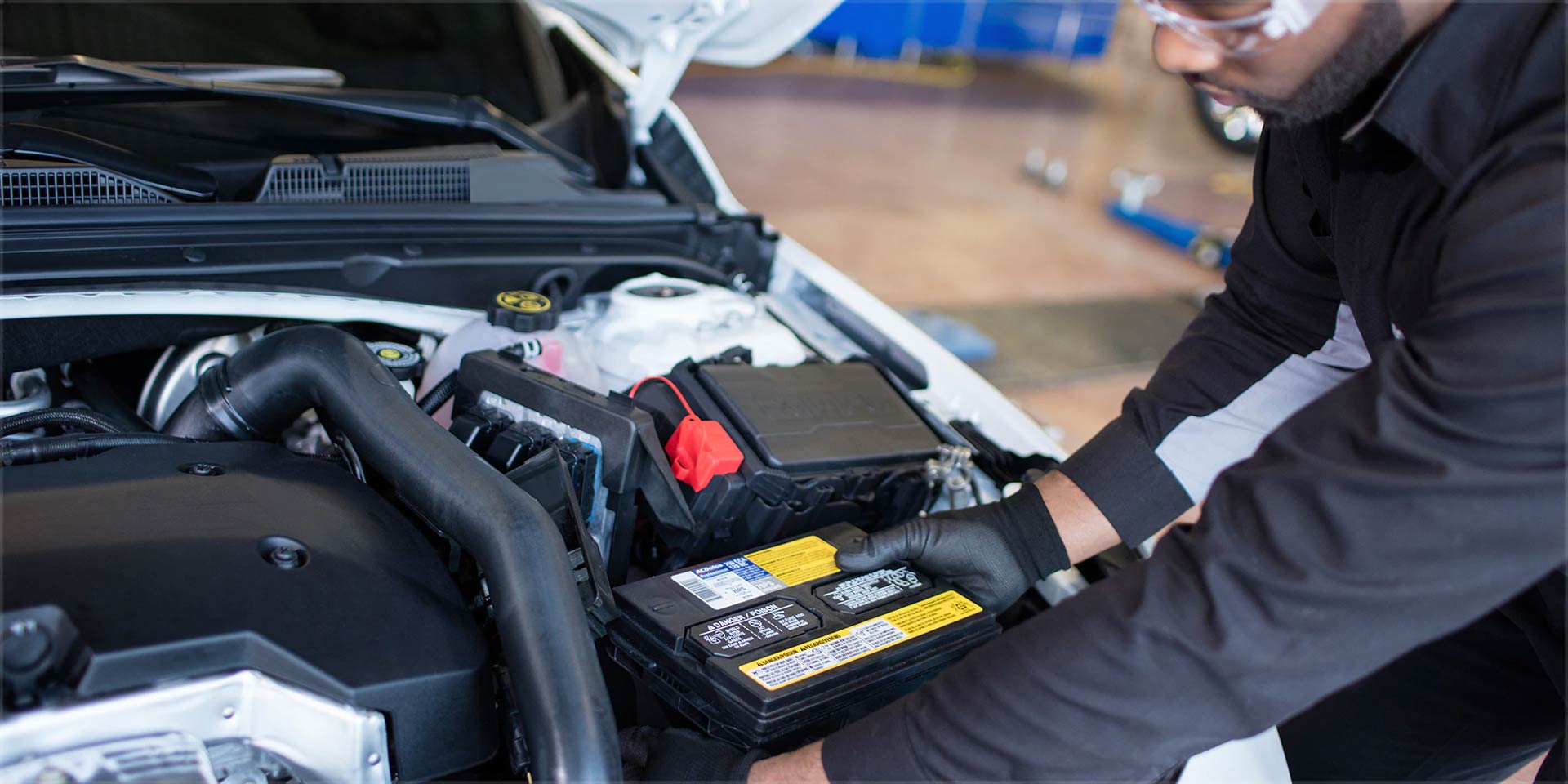Mechanic installing a new battery into a car engine bay.