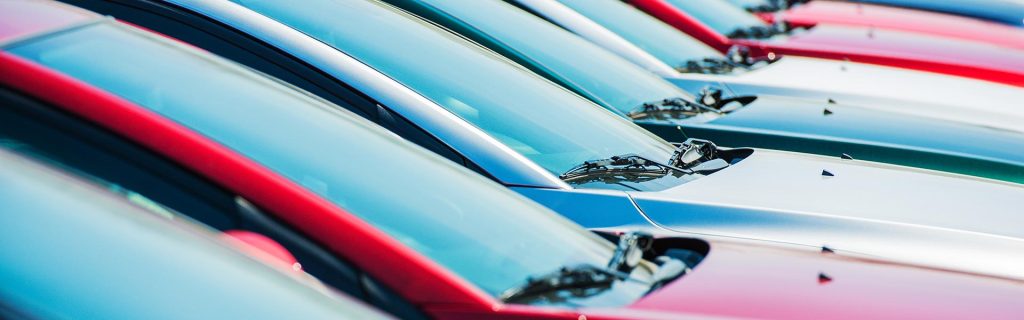 row of colorful cars lined up at a dealership lot.