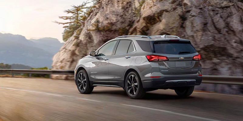 rear view of a gray 2024 chevy equinox driving on a road that his going trough mountain range